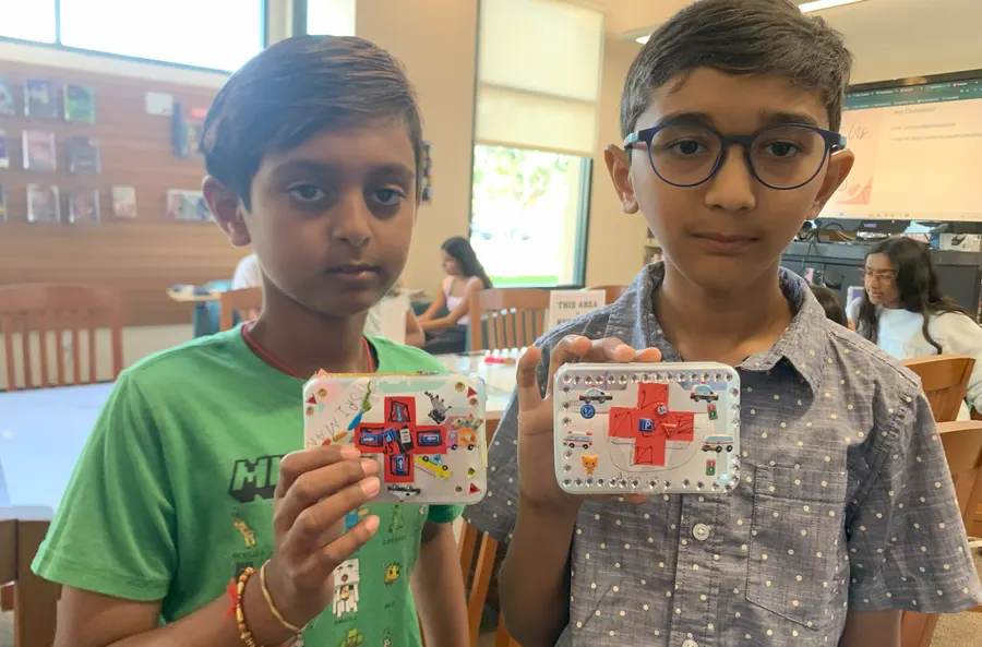 Two students hold up the first aid kits they packed and decorated