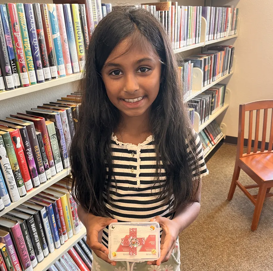 A student smiles holding her finished first aid kit in the library