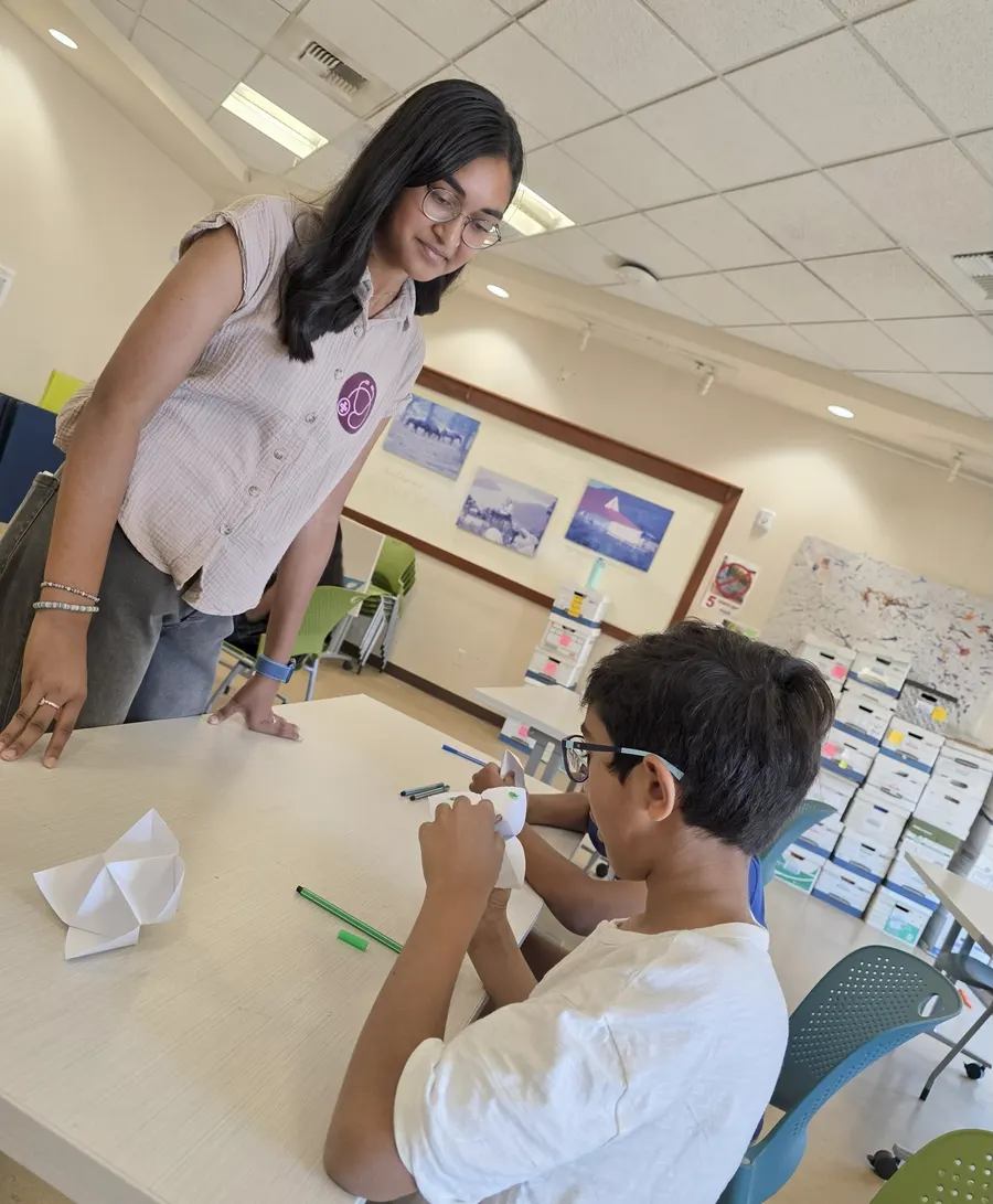 A volunteer helps a young student with the paper activity