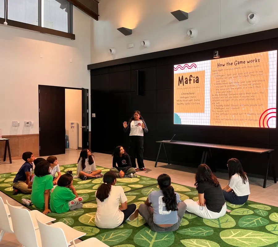 Children sit on the carpet while volunteers explain how the game works