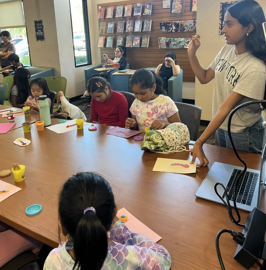 A volunteer helps a young student with her clay neuron