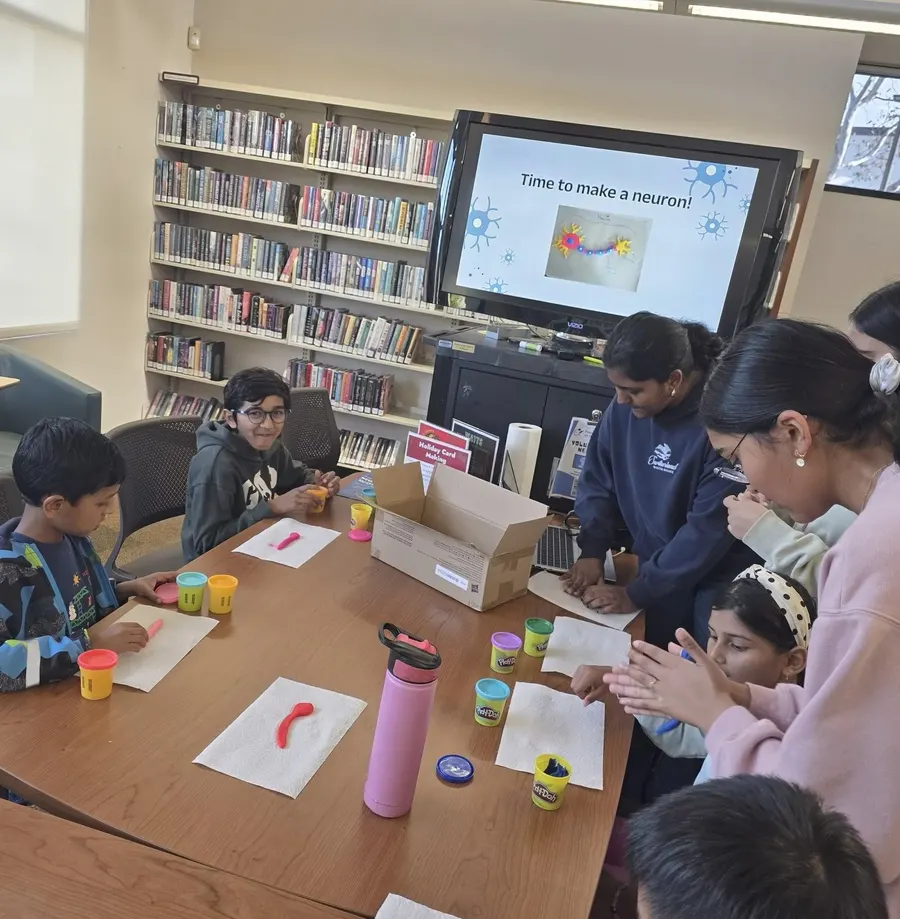Children build clay neurons while a slide reads 'Time to make a neuron!'
