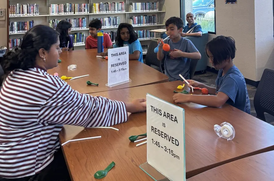 A volunteer hands out activity materials across the library table