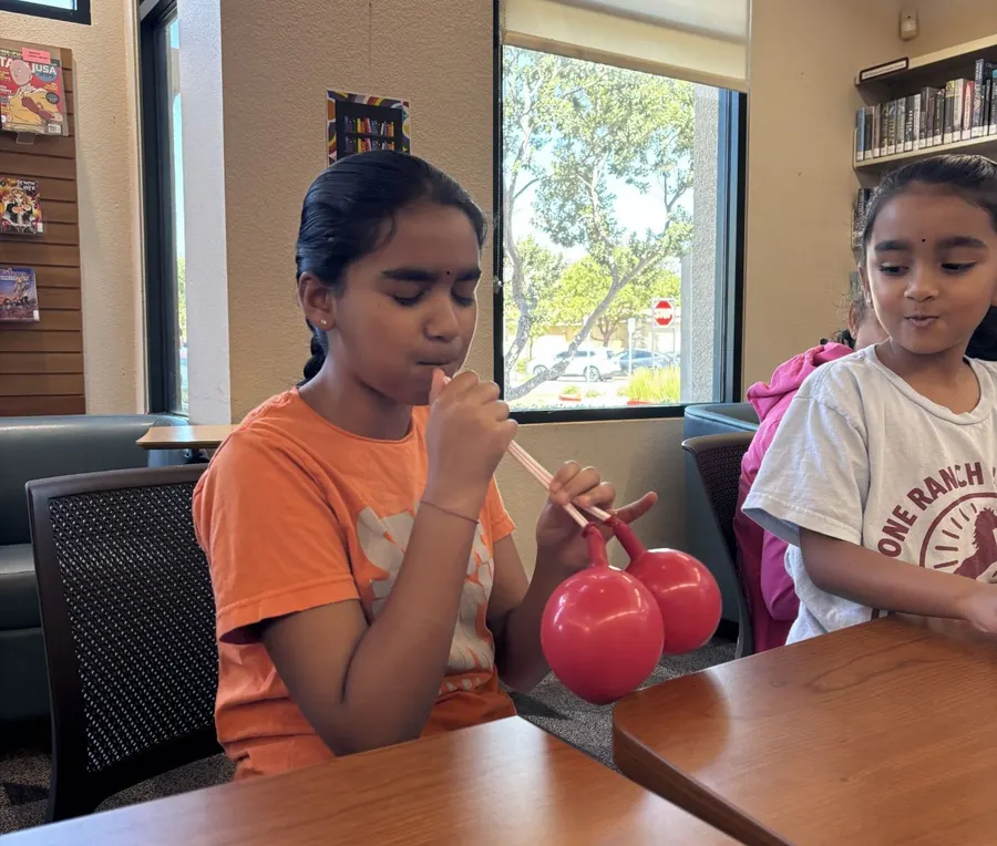 Two children at the table, one blowing up a red balloon to model a lung
