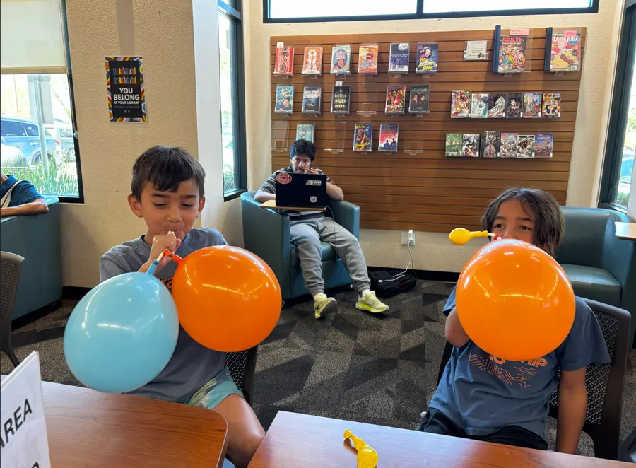 Two boys blow up blue and orange balloons to see how lungs fill with air
