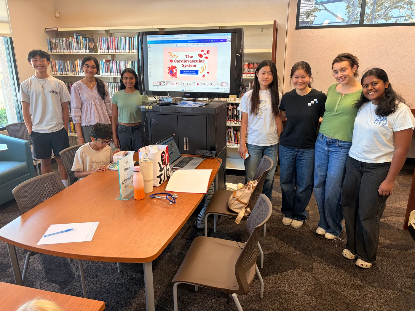 Eight ProjectPatho members at the 4s Ranch Library for the Cardiovascular System event, standing around the presentation screen and workshop table