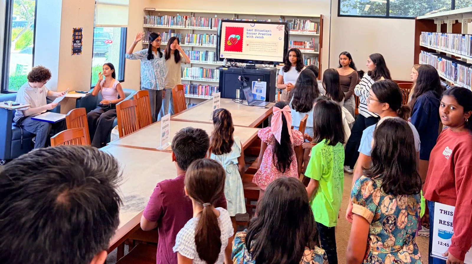 Children gathered around a ProjectPatho volunteer at the 4s Library as she walks them through a first aid scenario on screen
